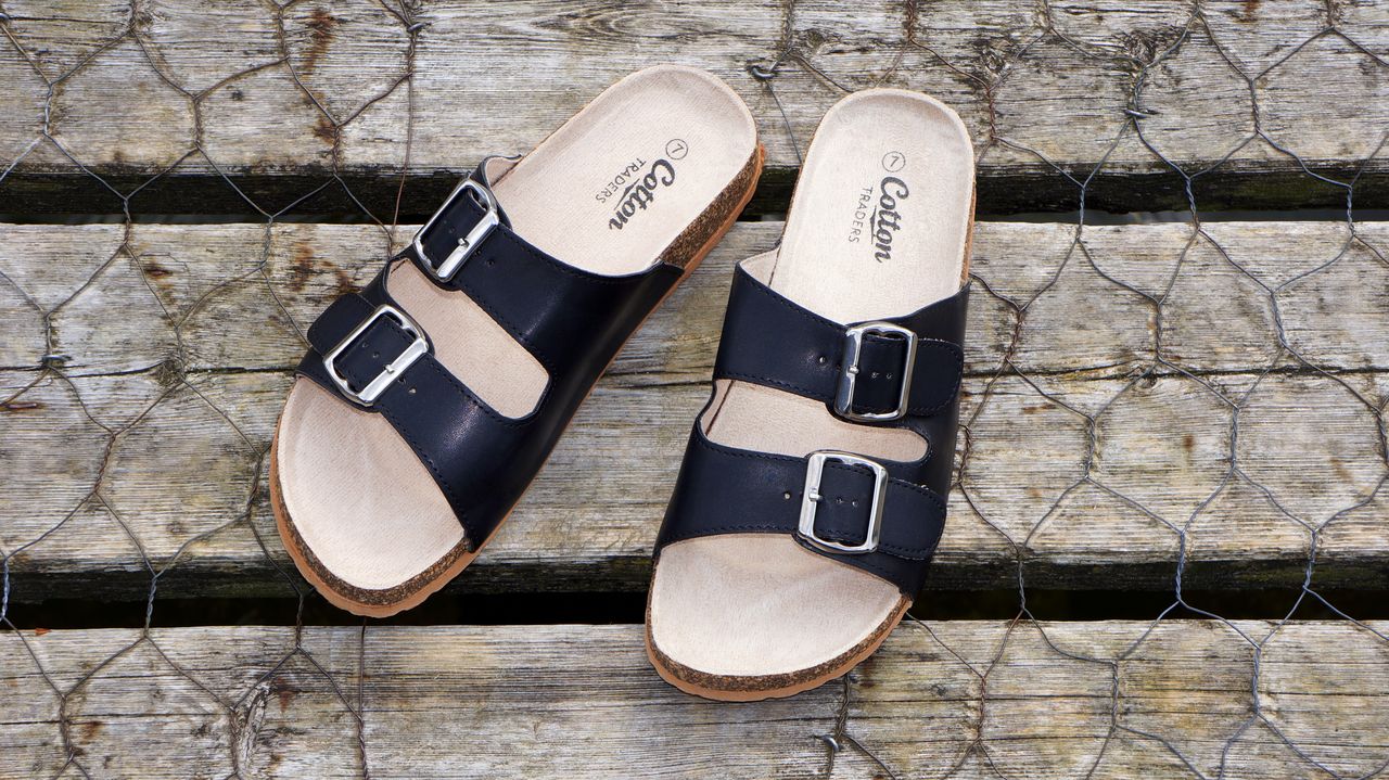 hero-img-01 Black leather buckle sandals on a wooden surface, perfect for casual summer fashion.